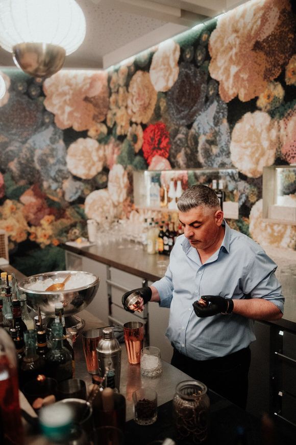 Barkeeper mixt Cocktails an einer eleganten Bar mit opulenter Blumendekoration – exquisites Ambiente zum heiraten im Morrhof.