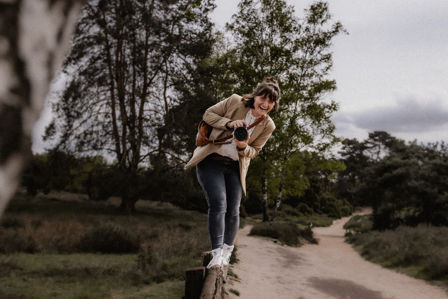 Photographer balances on wooden fence post along rural path.