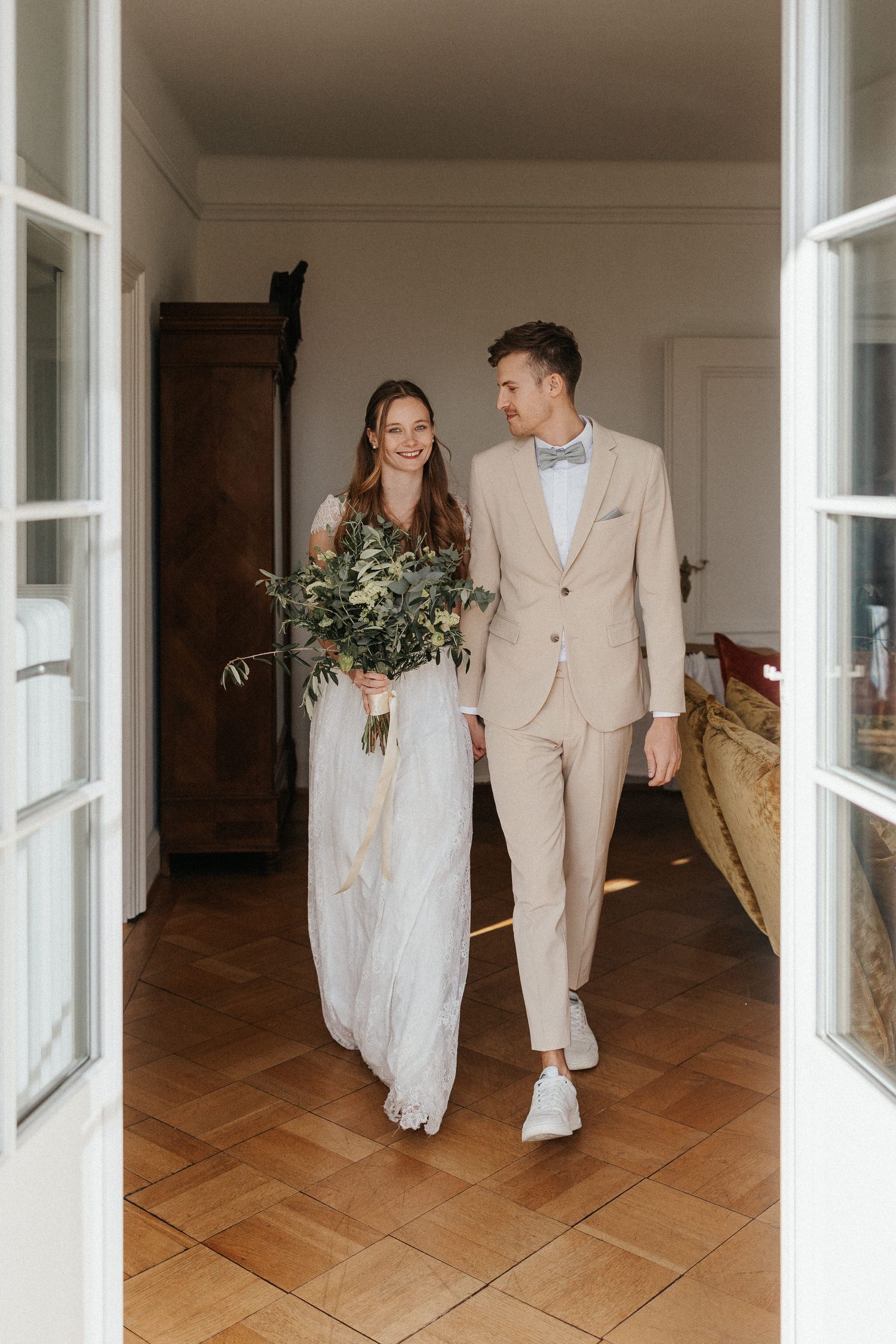 Wedding couple walks through elegant interior with herringbone wood flooring.