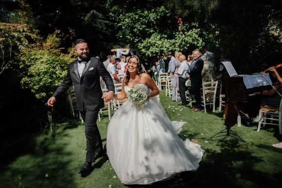 Hochzeitsfotograf Boudier & Koeller – Hochzeitsgesellschaft geht einen baumgesäumten Weg im Garten während der Outdoor-Zeremonie.