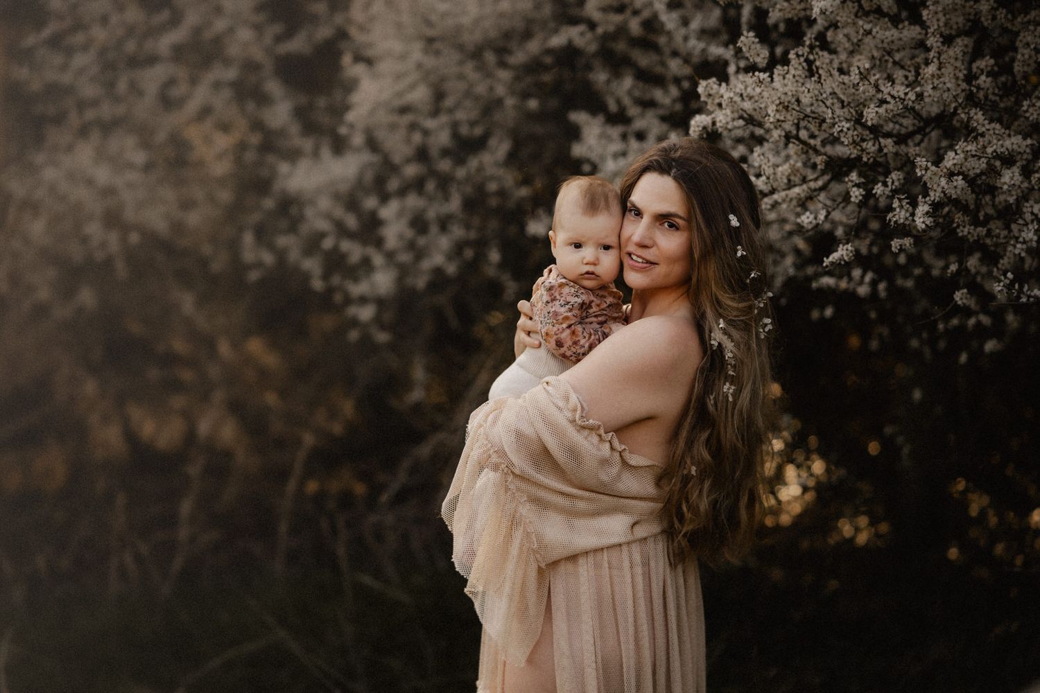 A romantic couple in neutral tones embraces in a dreamy outdoor setting during golden hour.