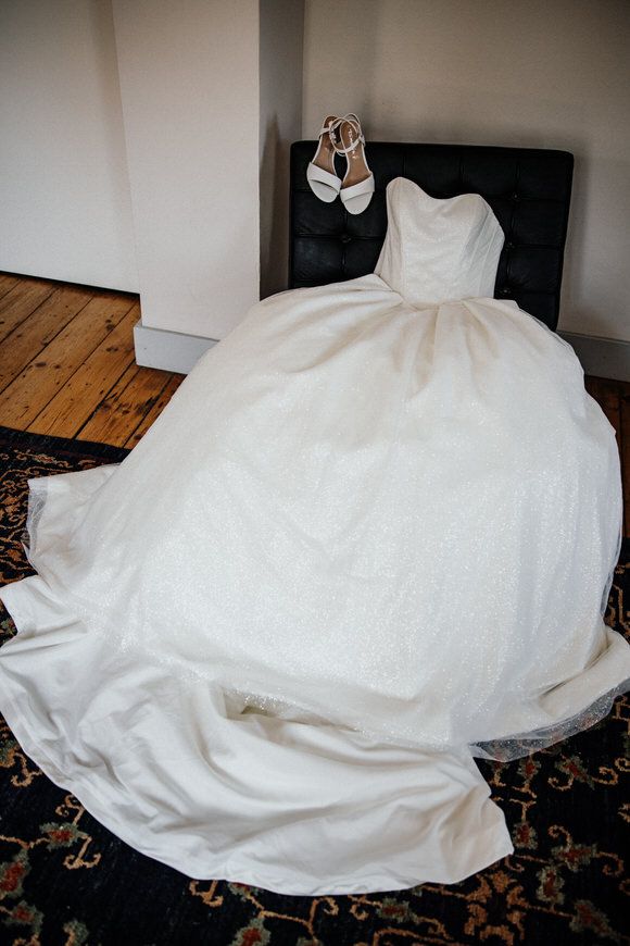 A flowing white wedding dress train with intricate details spreads across a patterned carpet.