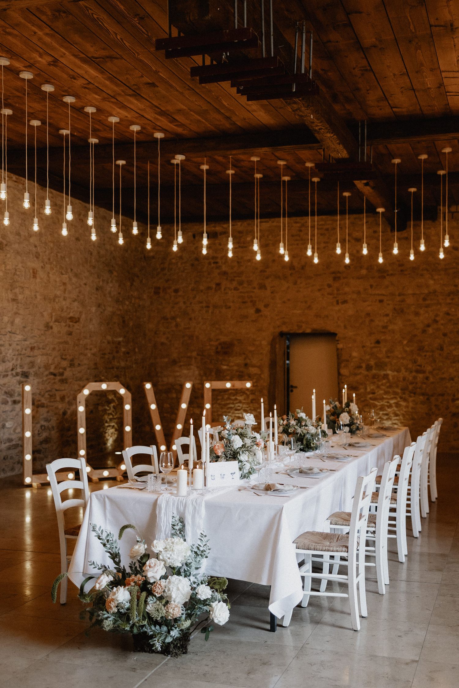Hochzeitsfotograf Boudier & Koeller – Rustikale Hochzeitslocation mit weißen Tischen, Lichterketten und Ziegelwänden.