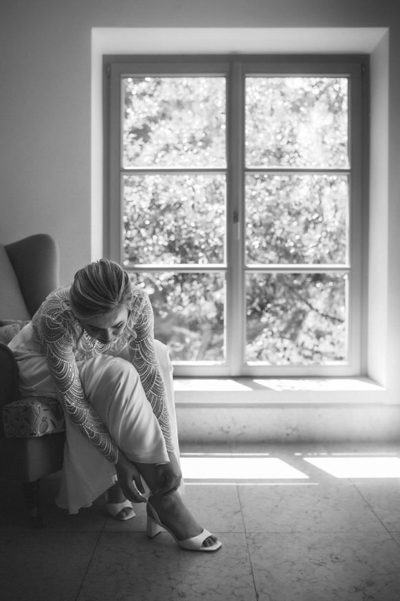 Schwarz-Weiß-Foto der Braut, die ihre Schuhe am Fenster in minimalistischem Ambiente richtet – stilvoll heiraten im Morrhof.