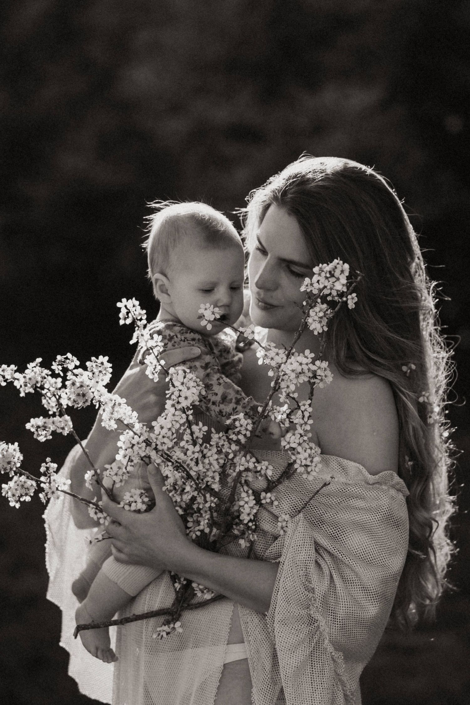 A tender black and white portrait series showing a parent and baby sharing sweet moments with delicate white flowers.