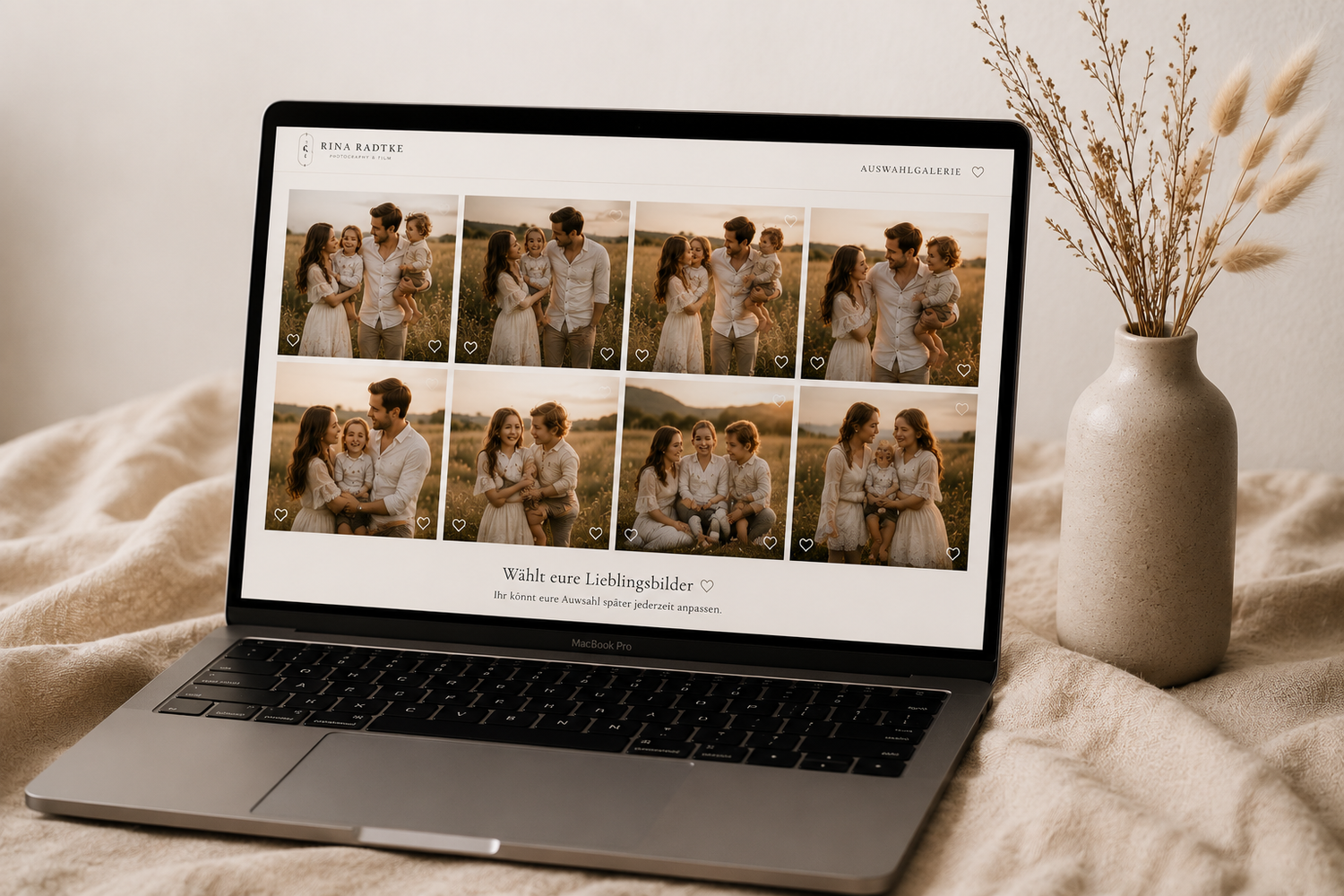 A laptop displaying a wedding photography website with a grid of romantic couple photos in warm tones, beside a dried floral arrangement.