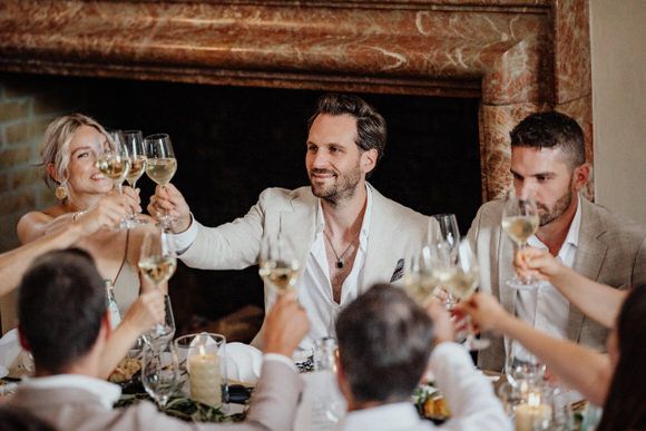 Hochzeitsfeier mit fröhlichen Gästen, die an einem rustikalen Ort anstoßen und feiern – stilvoll heiraten im Morrhof.