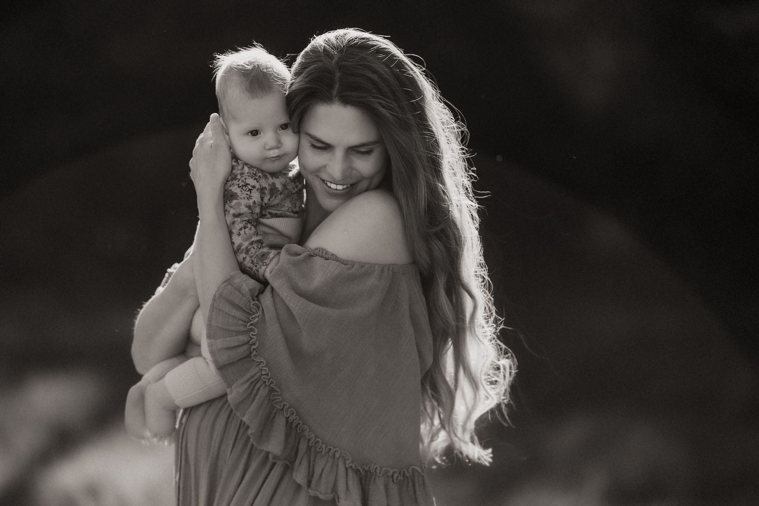 A parent and young child share a tender moment outdoors in black and white photography.