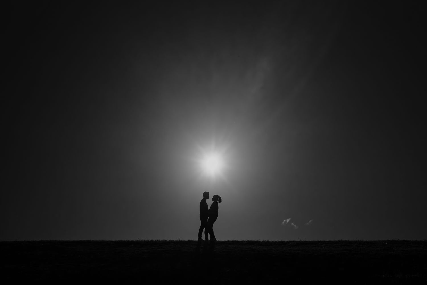 Black and white silhouette of a couple standing close together under a glowing light in a romantic night scene.