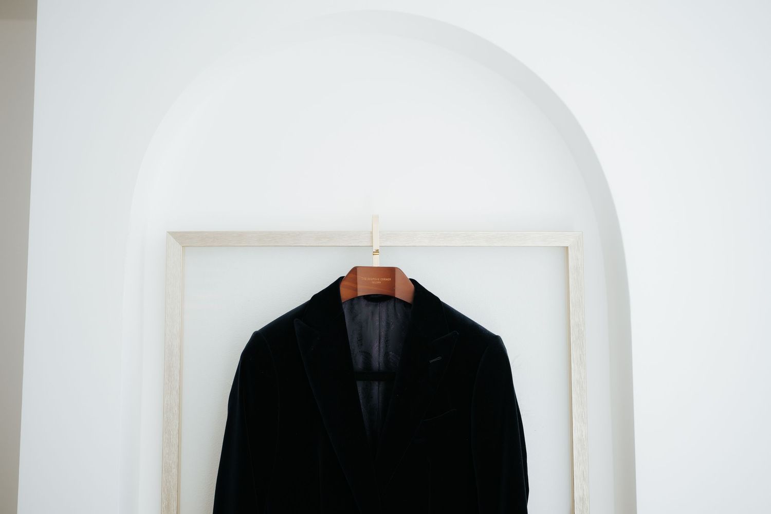 Black velvet blazer hanging on a wooden hanger in a white arched doorway.