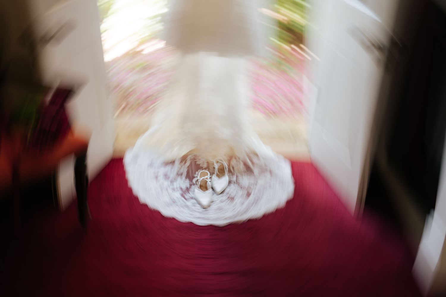 Blurred wedding dress displayed on a red table with rings, captured with artistic zoom effect.