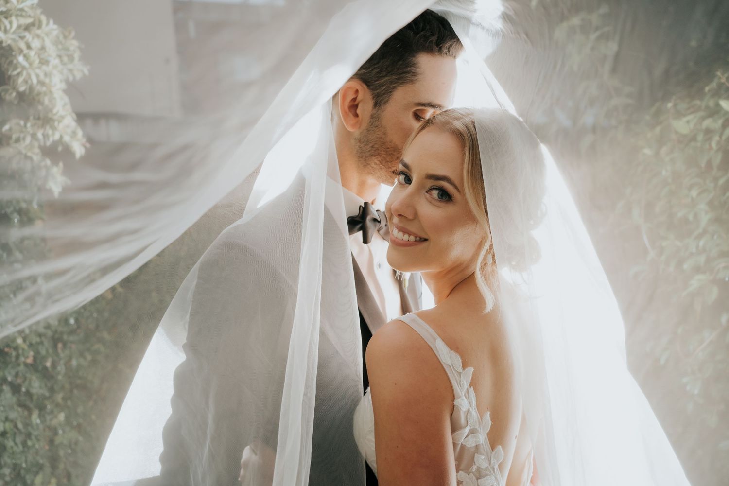 Bride and groom share an intimate moment under a flowing white veil on their wedding day.