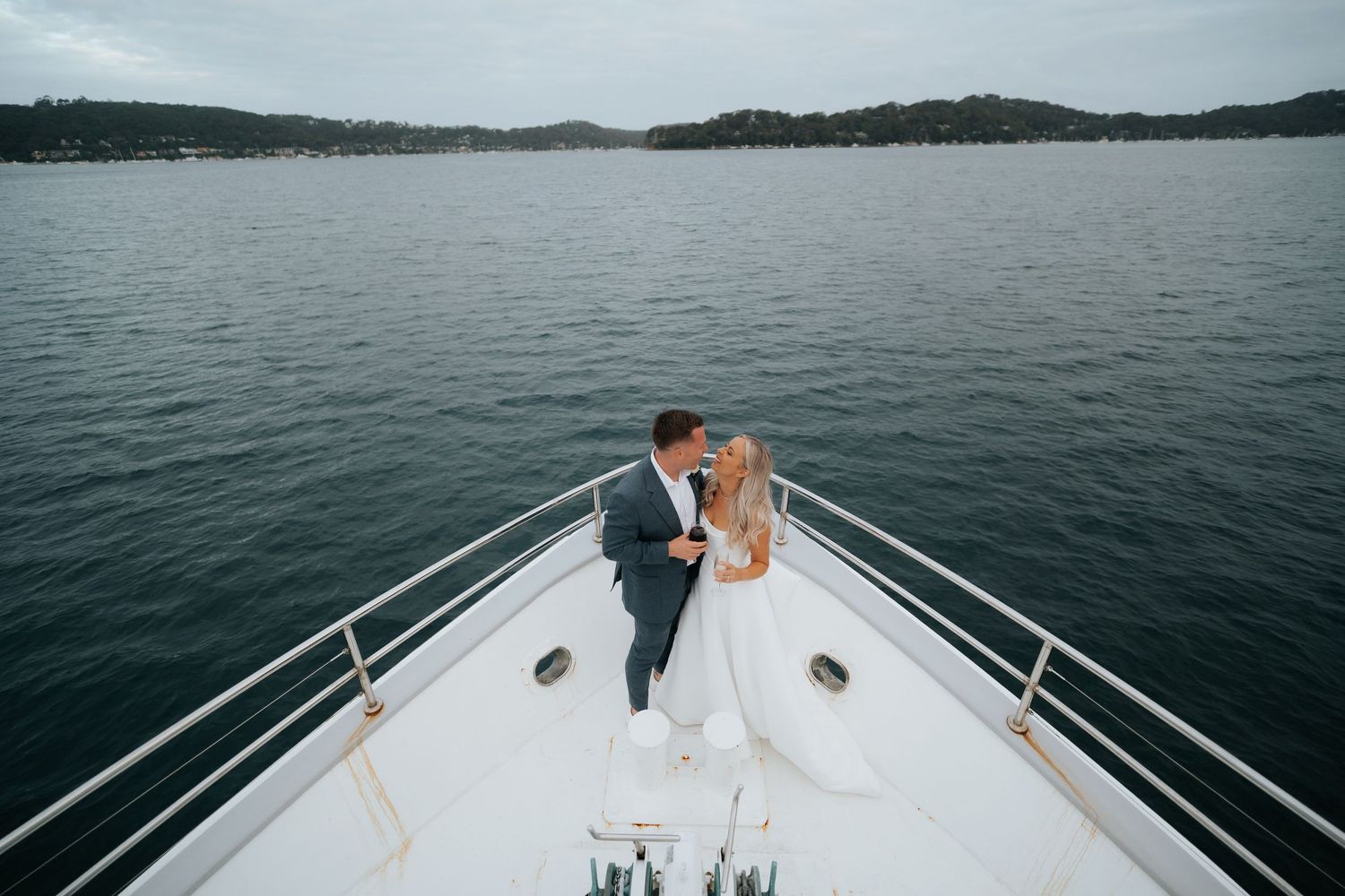 Bride and groom share a romantic kiss on the bow of a luxury yacht on a calm lake.