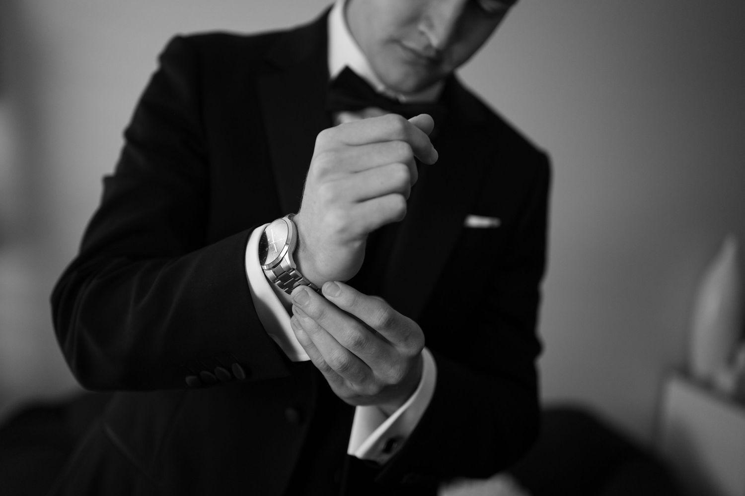 Black and white photo of a groom in a tuxedo adjusting his cufflinks and watch before his wedding.