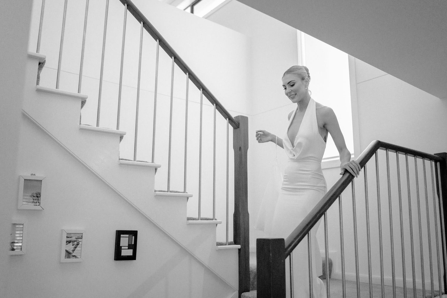 Woman in elegant white dress descending modern staircase in black and white photo.