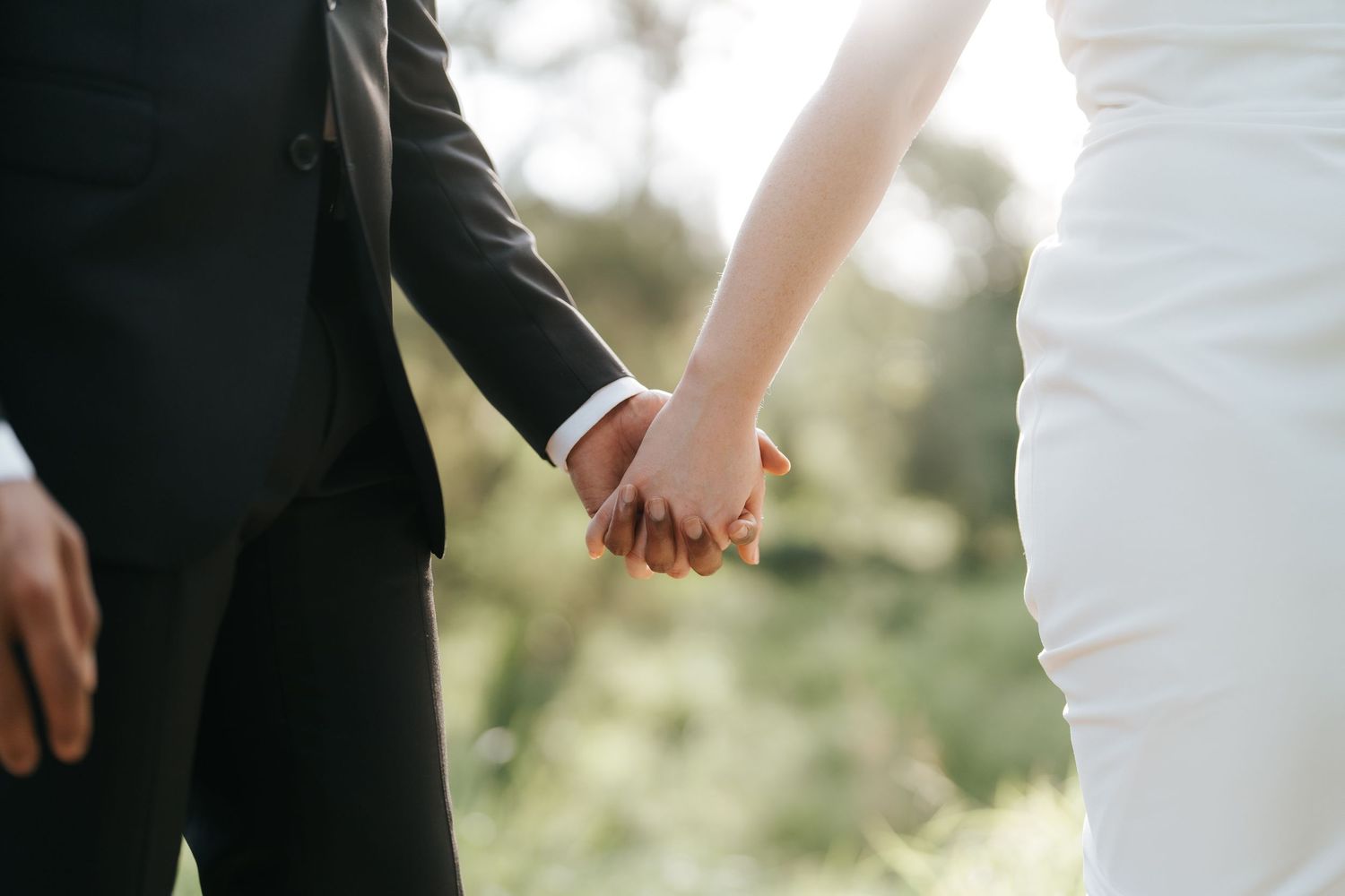 Bride and groom holding hands outdoors on wedding day, wearing white dress and black tuxedo.
