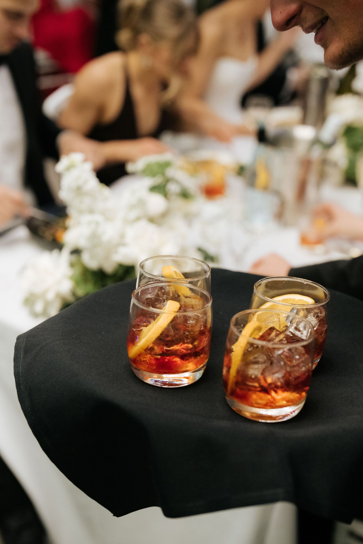 Two cocktails garnished with orange slices and ice served on a black linen table at a wedding reception.