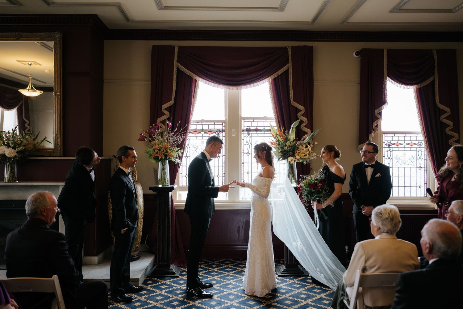 Bride and groom exchanging vows in intimate indoor ceremony with elegant purple draped windows.
