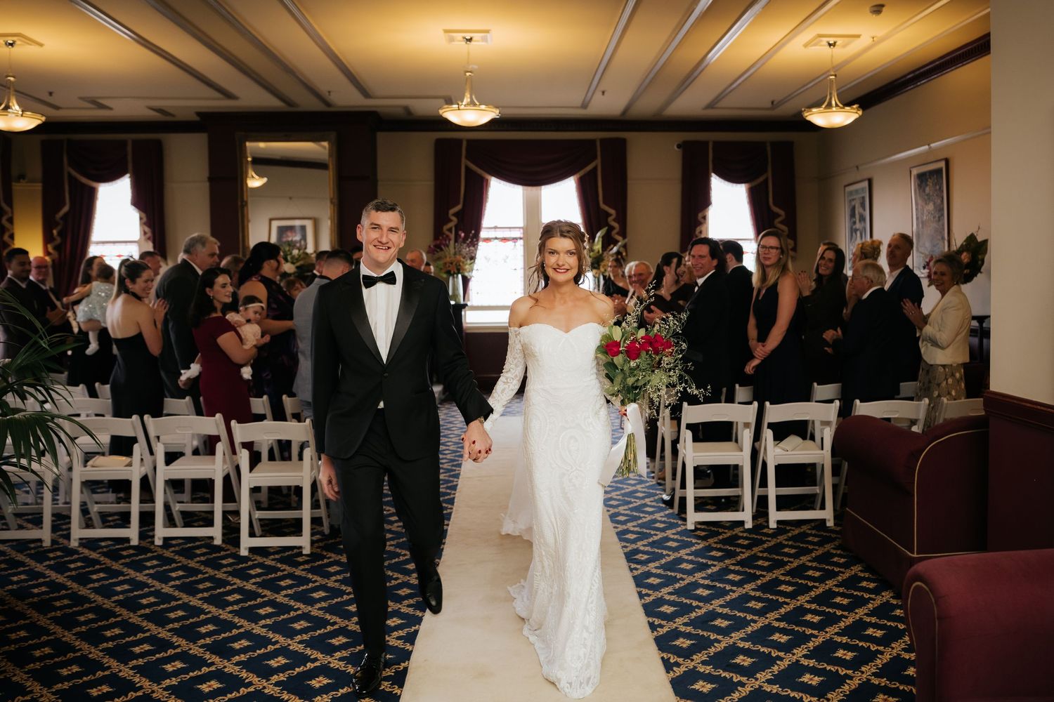 Bride and groom walk down the aisle hand in hand after wedding ceremony in elegant indoor venue.