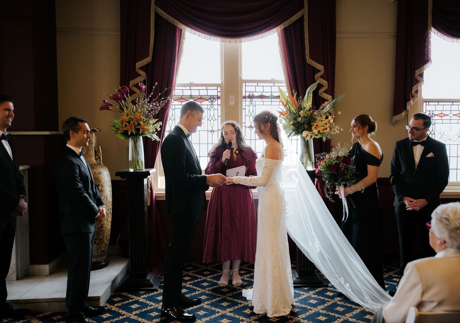 Elegant wedding ceremony with bride in white gown exchanging vows, flanked by wedding party in purple and black formal attire.