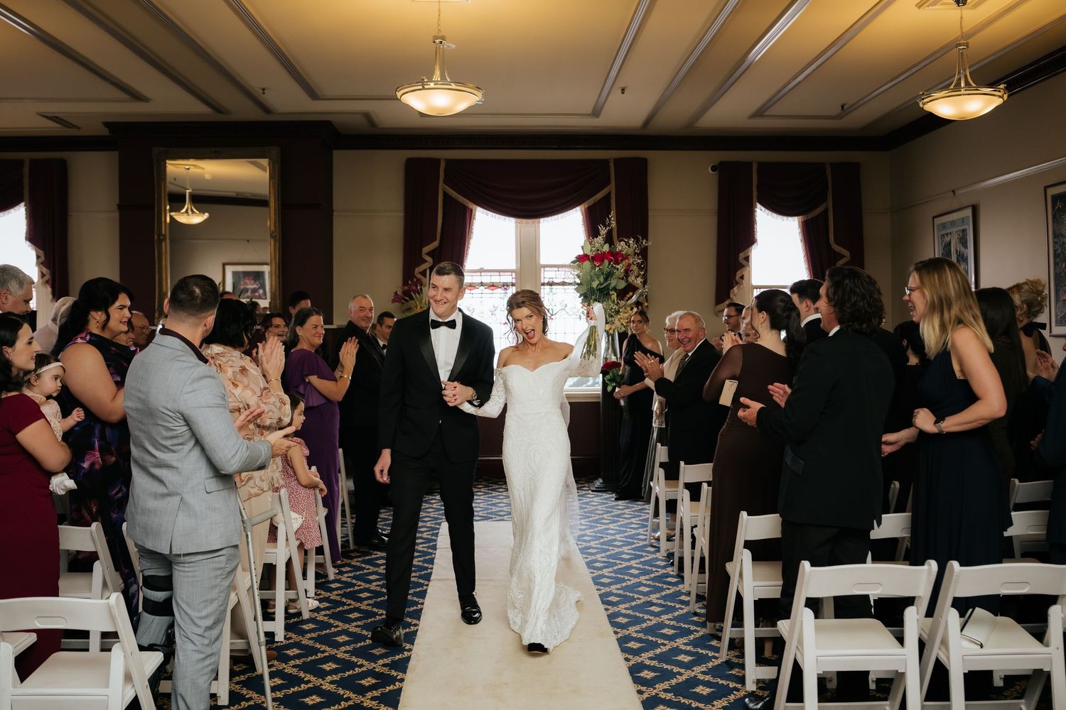 Newlyweds walk down the aisle together after wedding ceremony as guests celebrate in elegant venue.