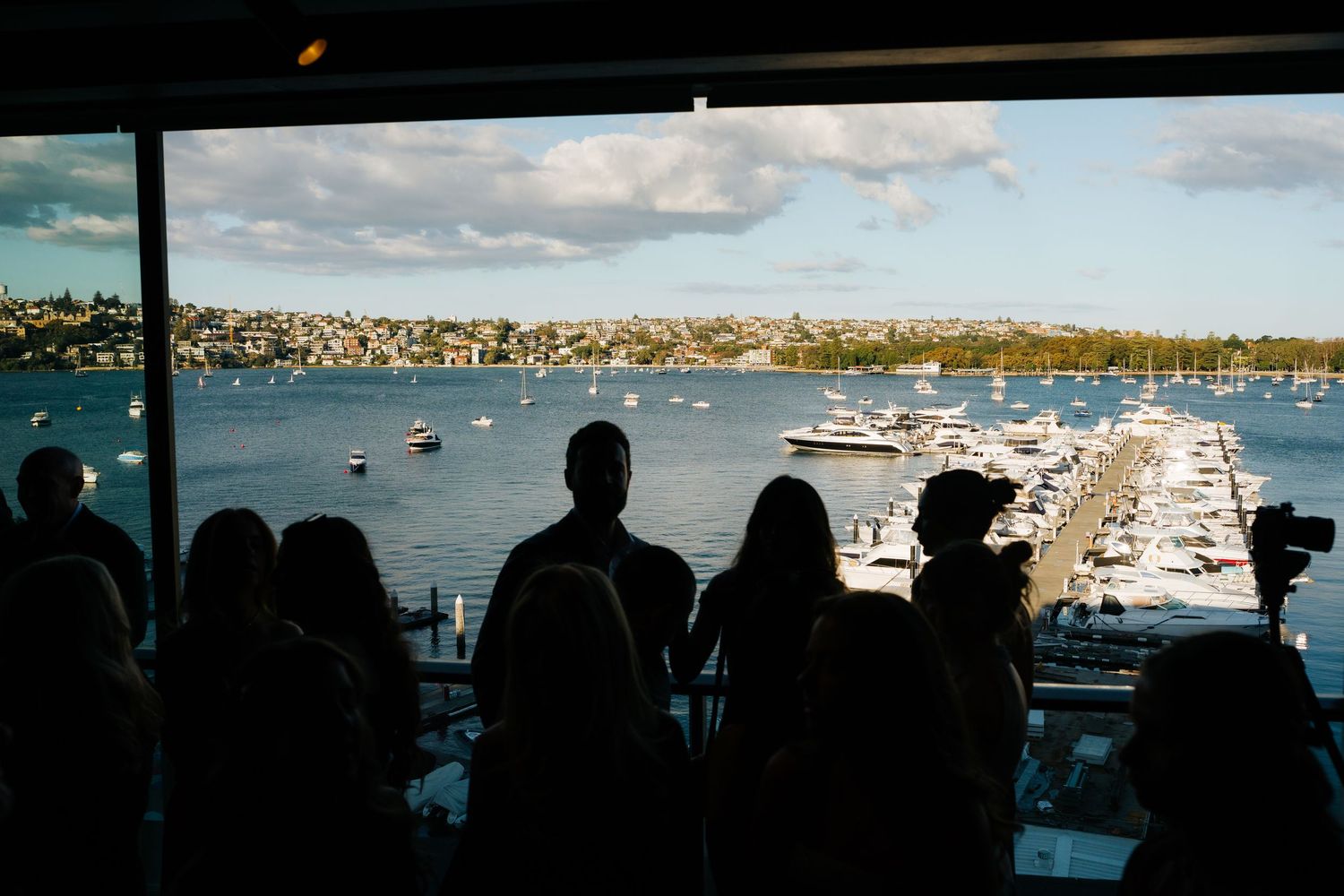 Silhouettes of people overlooking a marina and cityscape from a window.