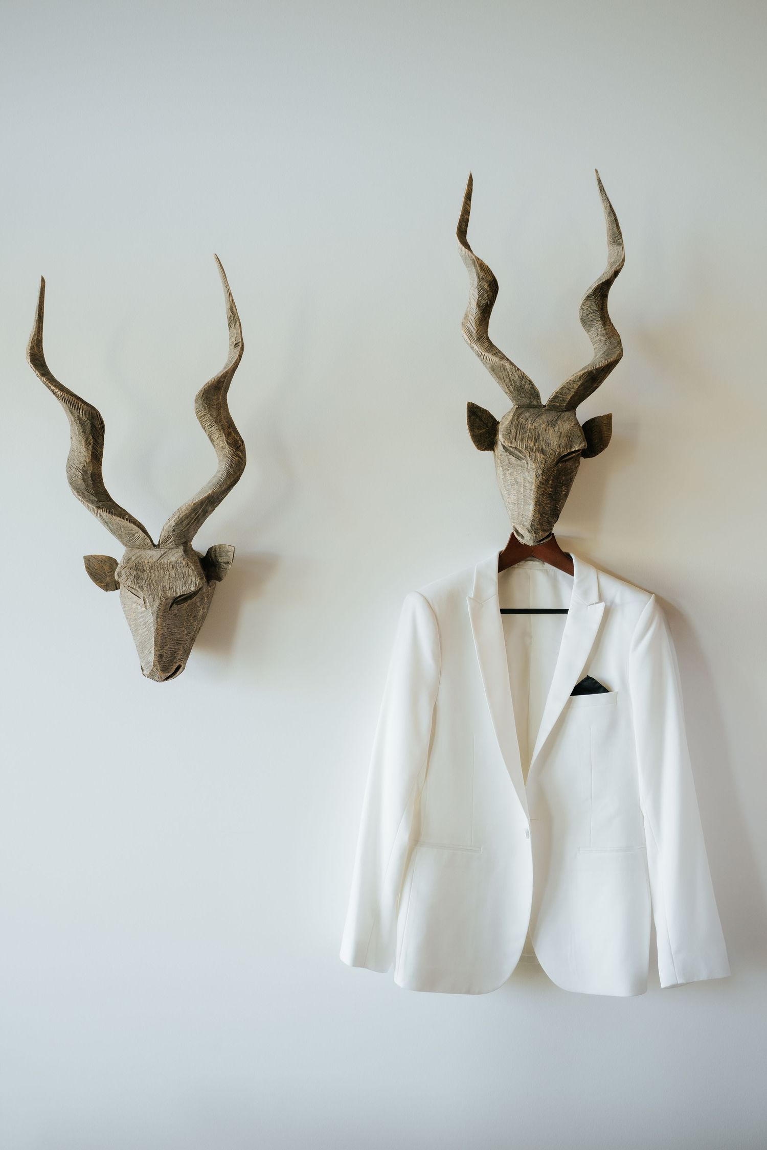 White blazer with bow tie hanging on decorative antelope trophy mount on white wall.