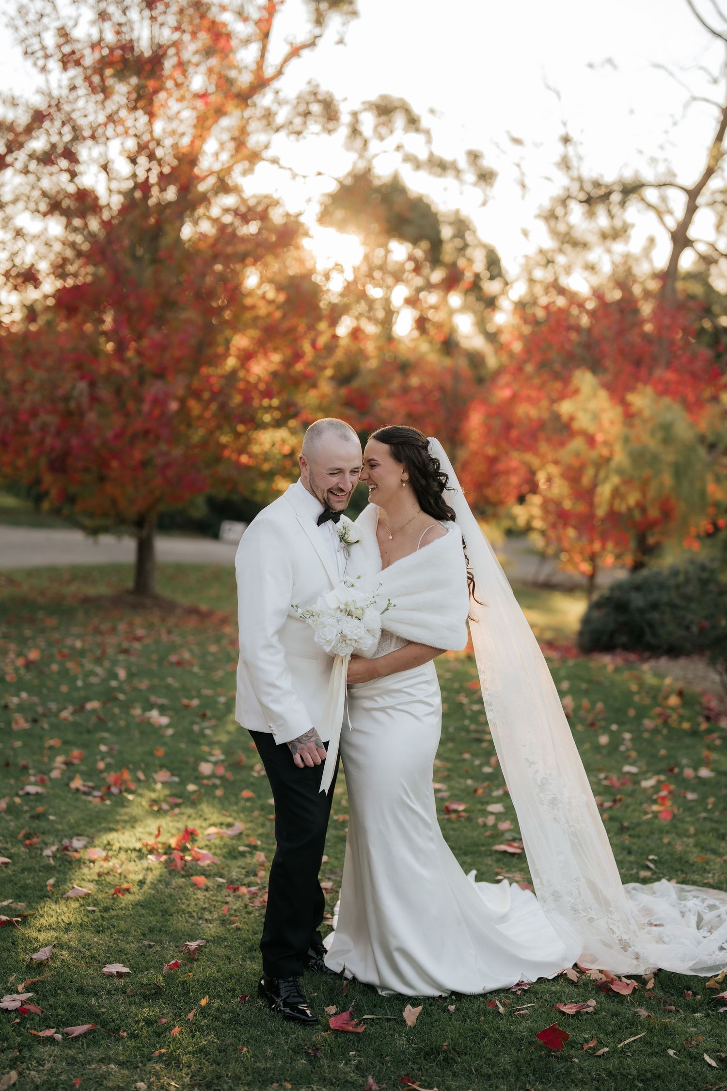 Bride and groom sharing romantic moment surrounded by vibrant red autumn foliage at golden hour.