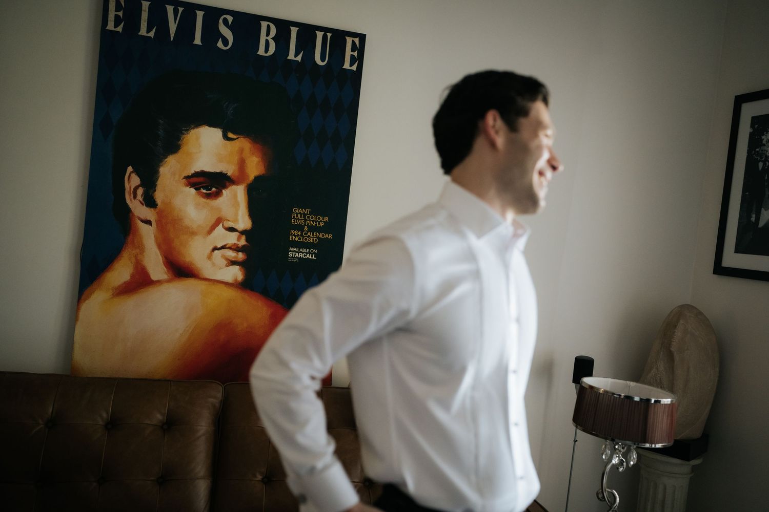 Man in white dress shirt standing near an Elvis Blue movie poster in a modern room.