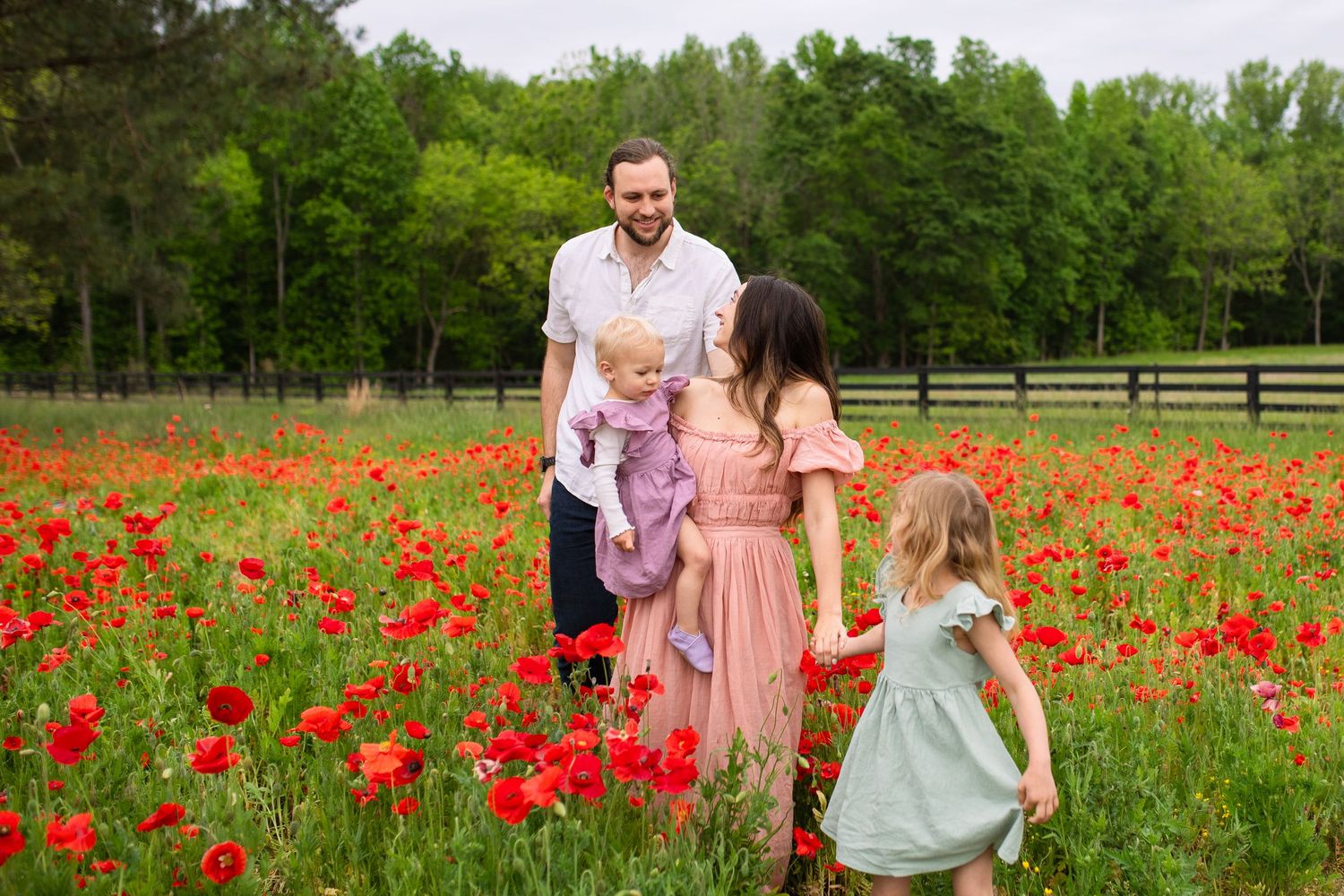 A family walks through a vibrant field of red poppies on a spring day with lush green trees in the background in Raleigh, NC