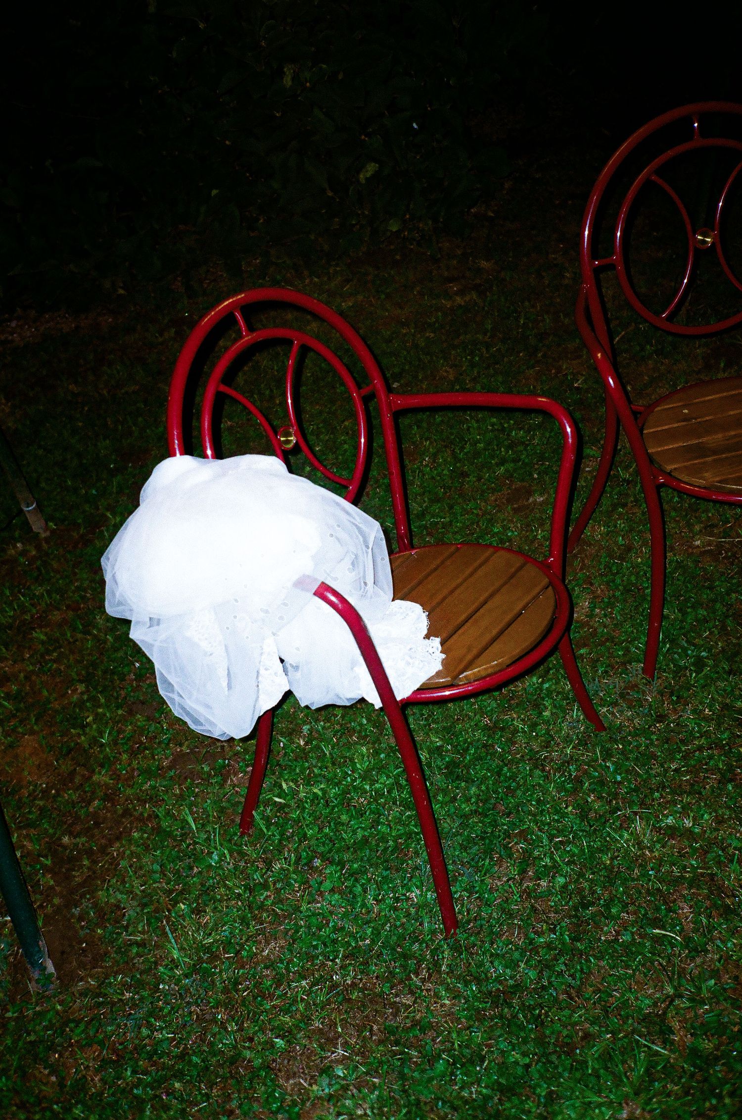 Red metal chairs arranged on grass under string lights at a nighttime outdoor event.