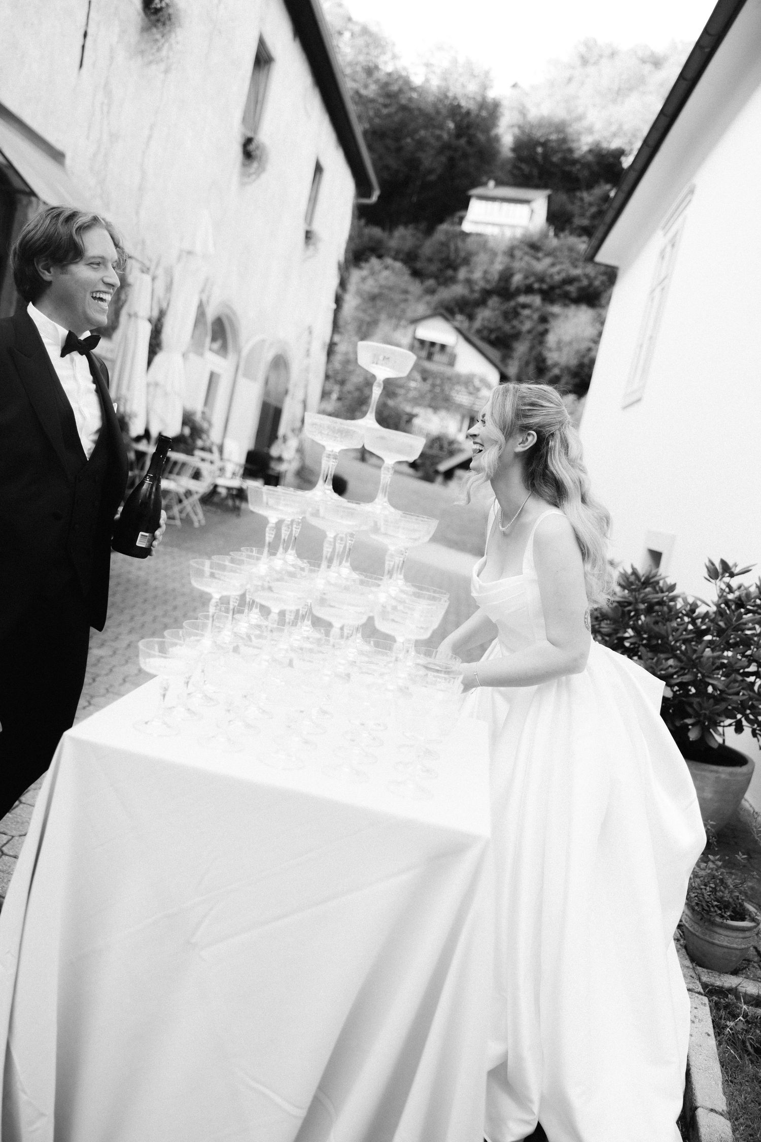 Wedding reception guests gather around an elegant white-clothed table with wine glasses and place settings.
