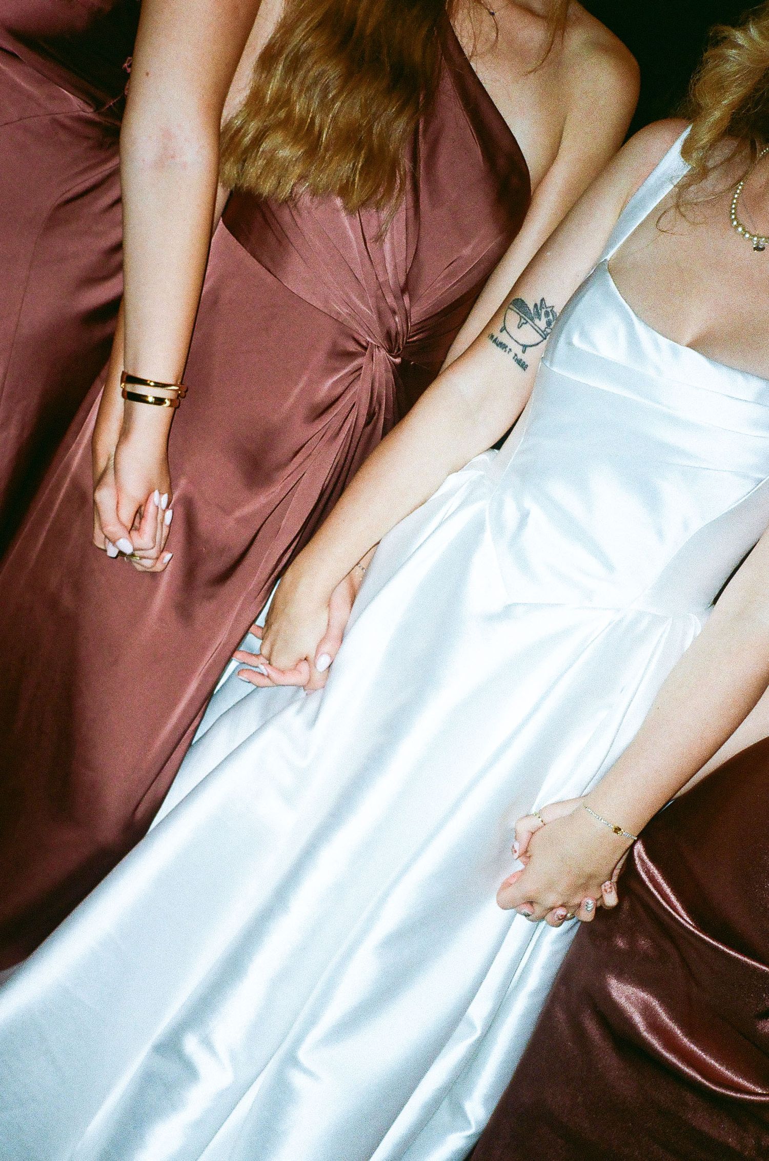 Hands holding and adjusting a white wedding dress next to burgundy bridesmaid dresses during wedding preparations.