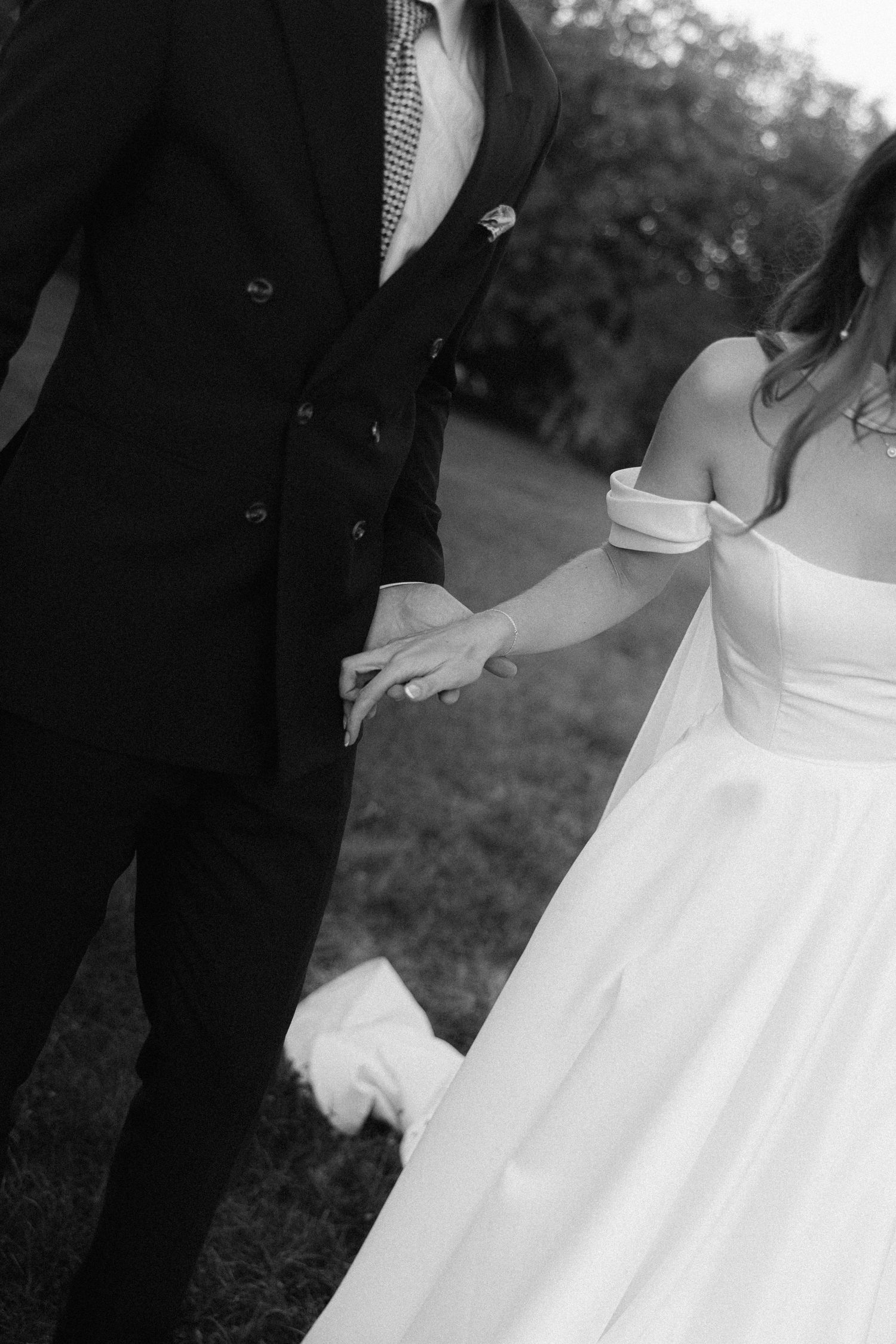 A series of black and white wedding photos showing details of a bride's white dress and groom's suit during an outdoor ceremony.