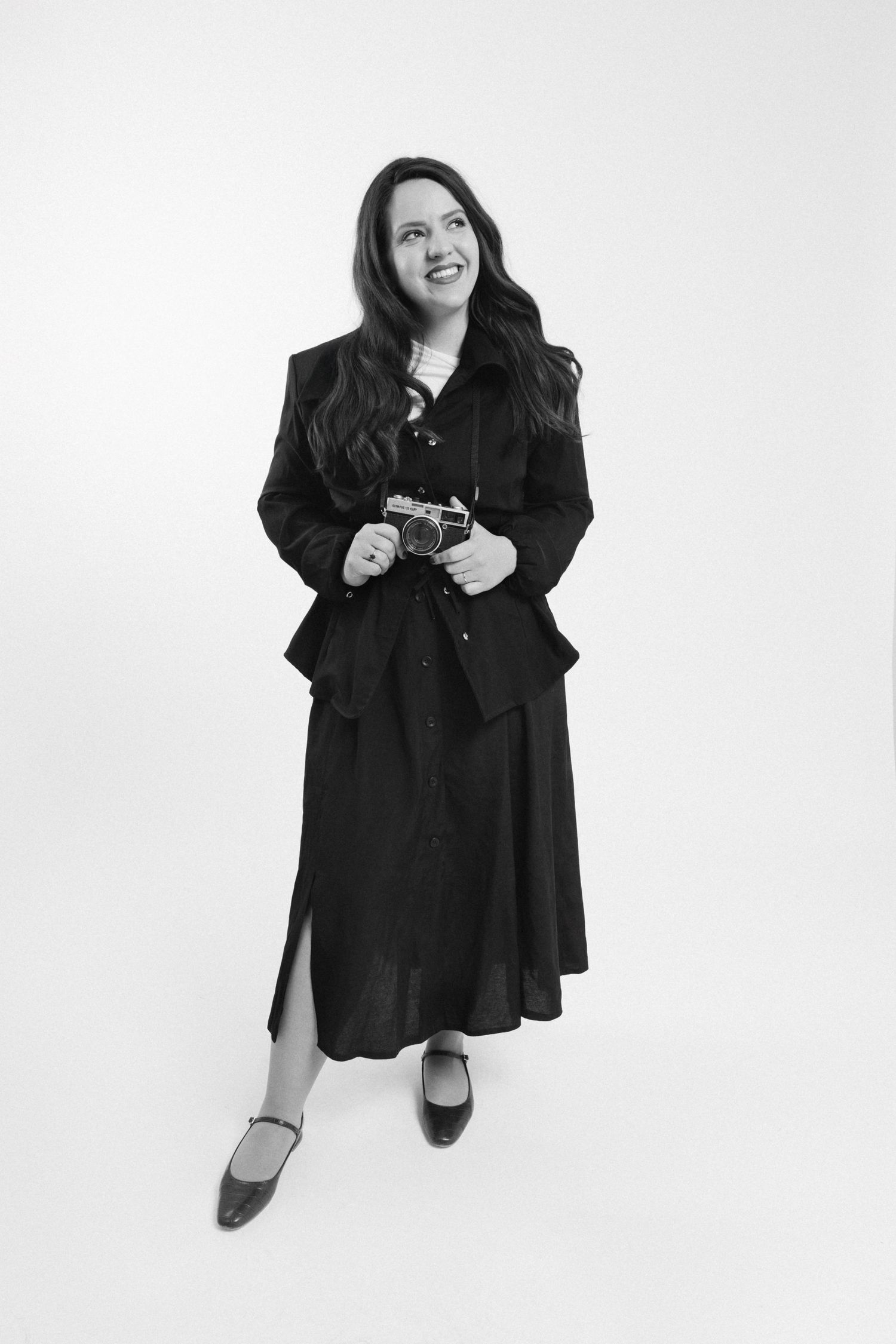 A person in a black outfit sits and poses playfully against a white backdrop in a series of three photos.