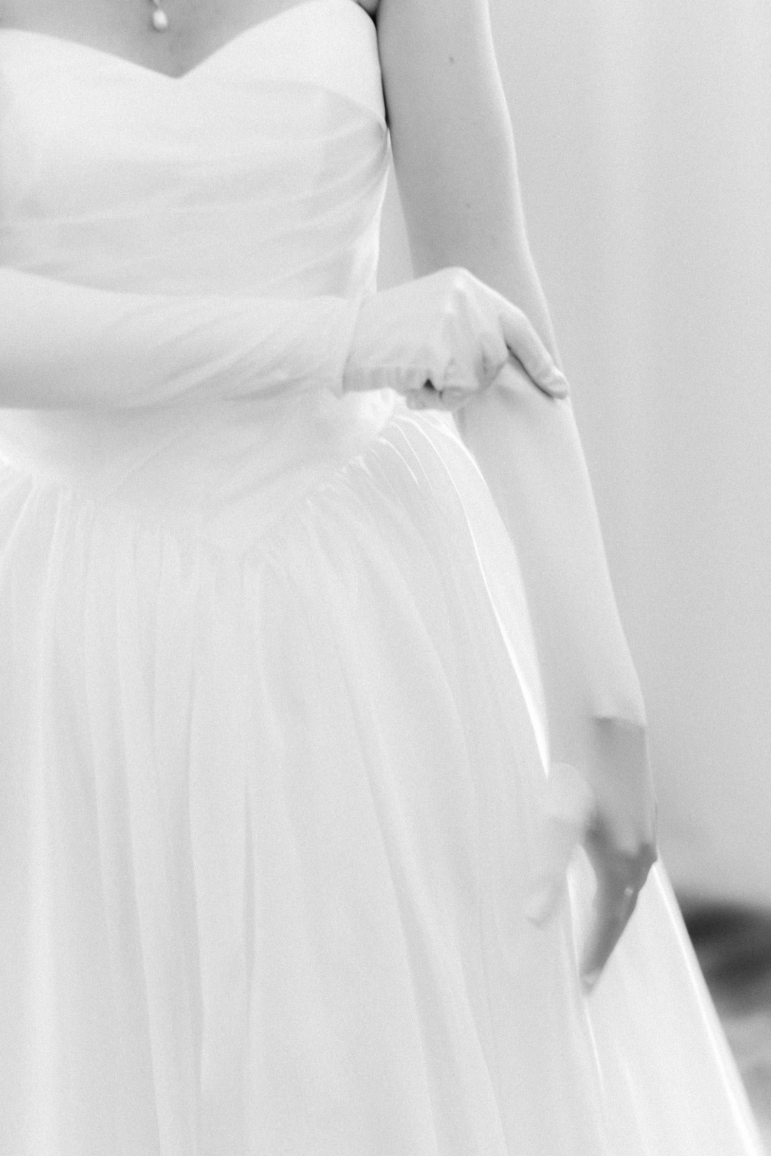 Close-up details of a white wedding dress showing delicate fabric and elegant draping in a black and white photograph.