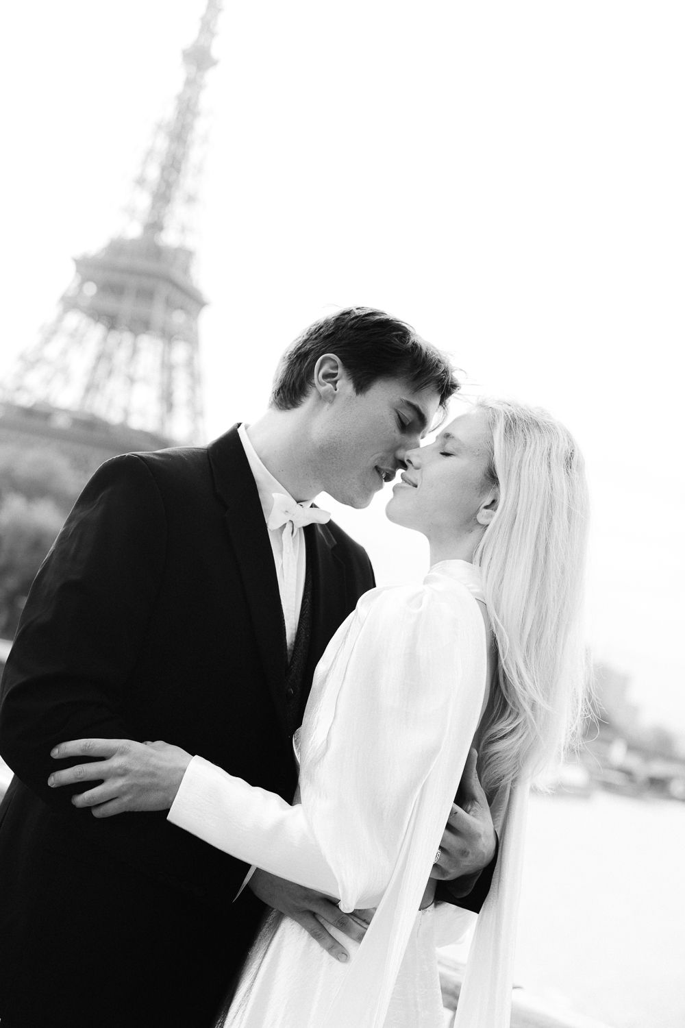 A romantic black and white wedding photo with a couple kissing in front of the Eiffel Tower in Paris.