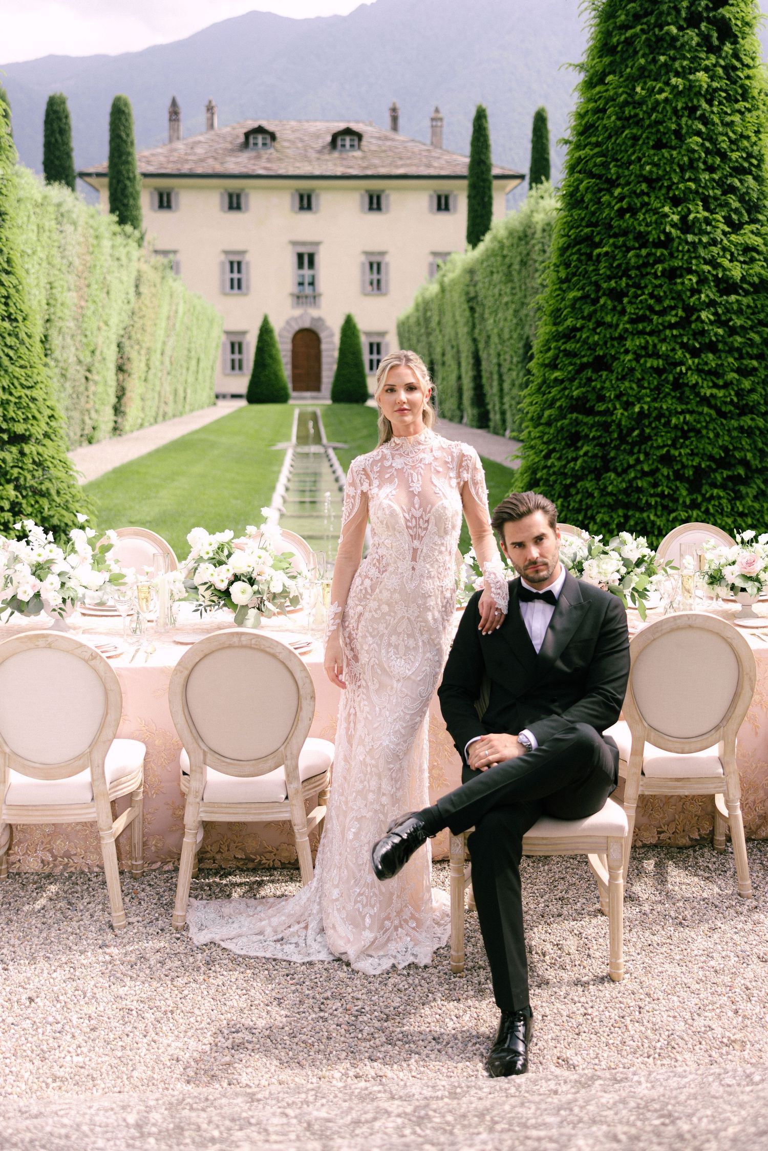 Elegant wedding setup at an Italian villa with cypress trees and white floral decor on a gravel path.