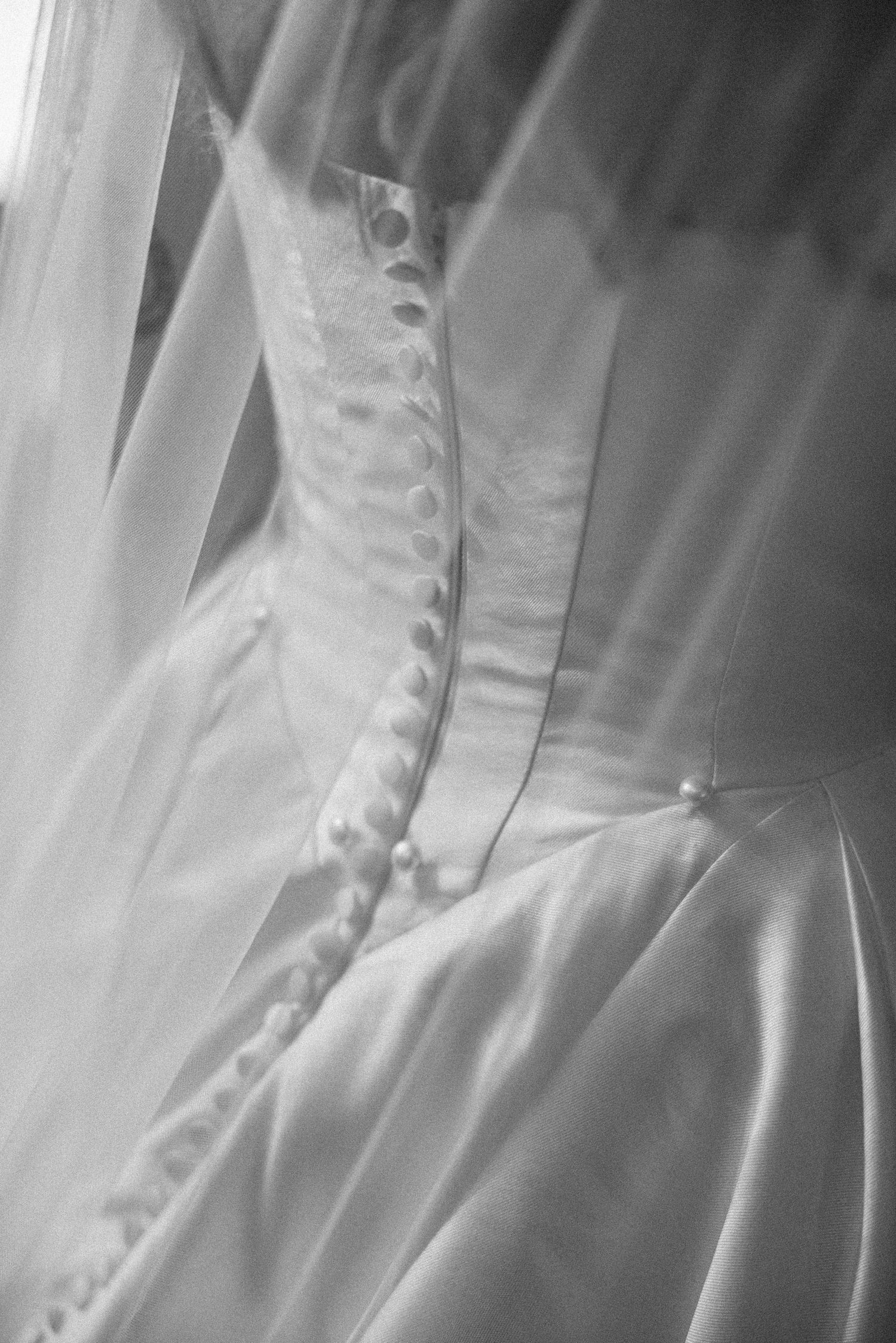 Close-up details of a white wedding dress showing delicate buttons and fabric texture in black and white photography.