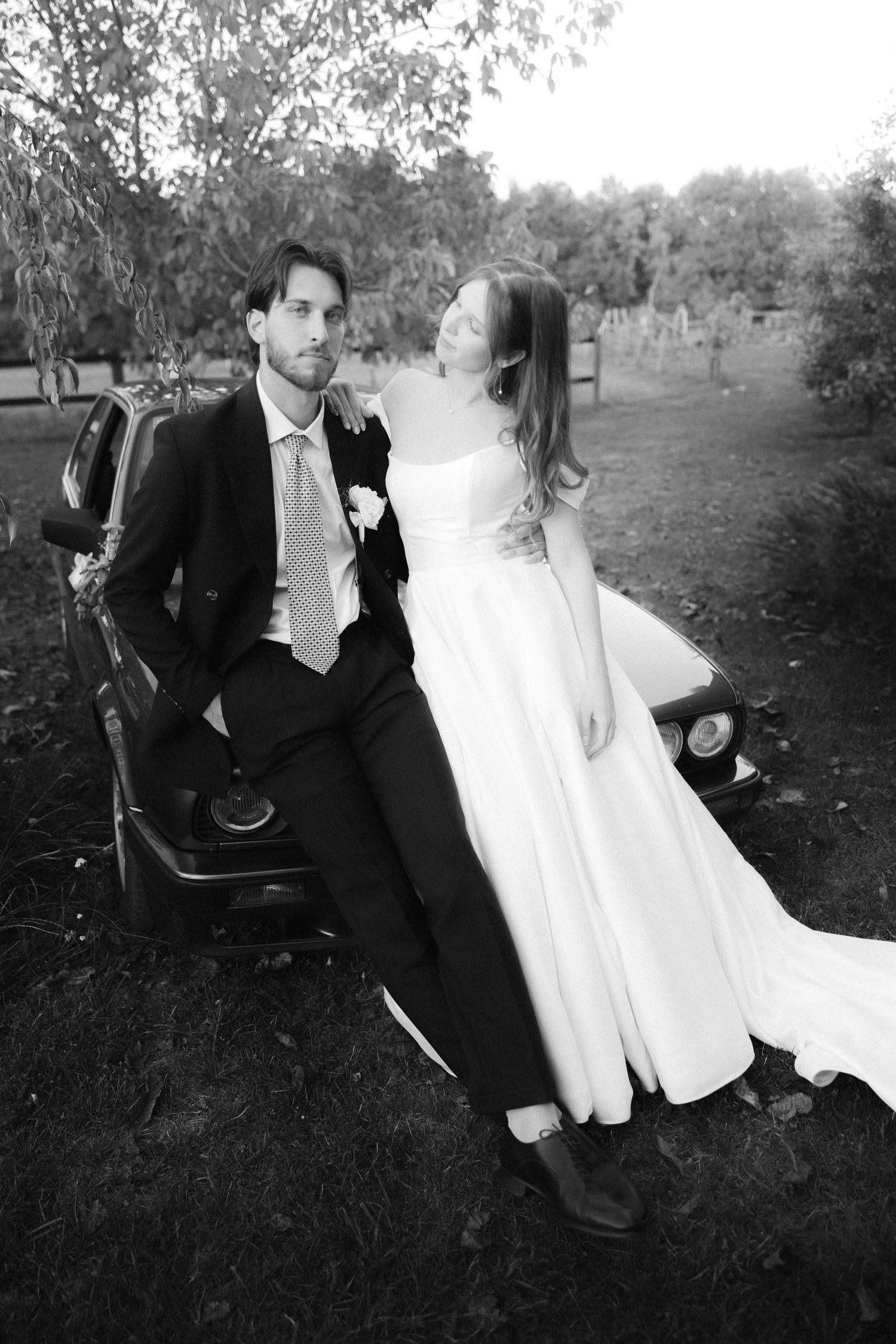A couple in formal wedding attire poses together outdoors in a romantic black and white photo series.