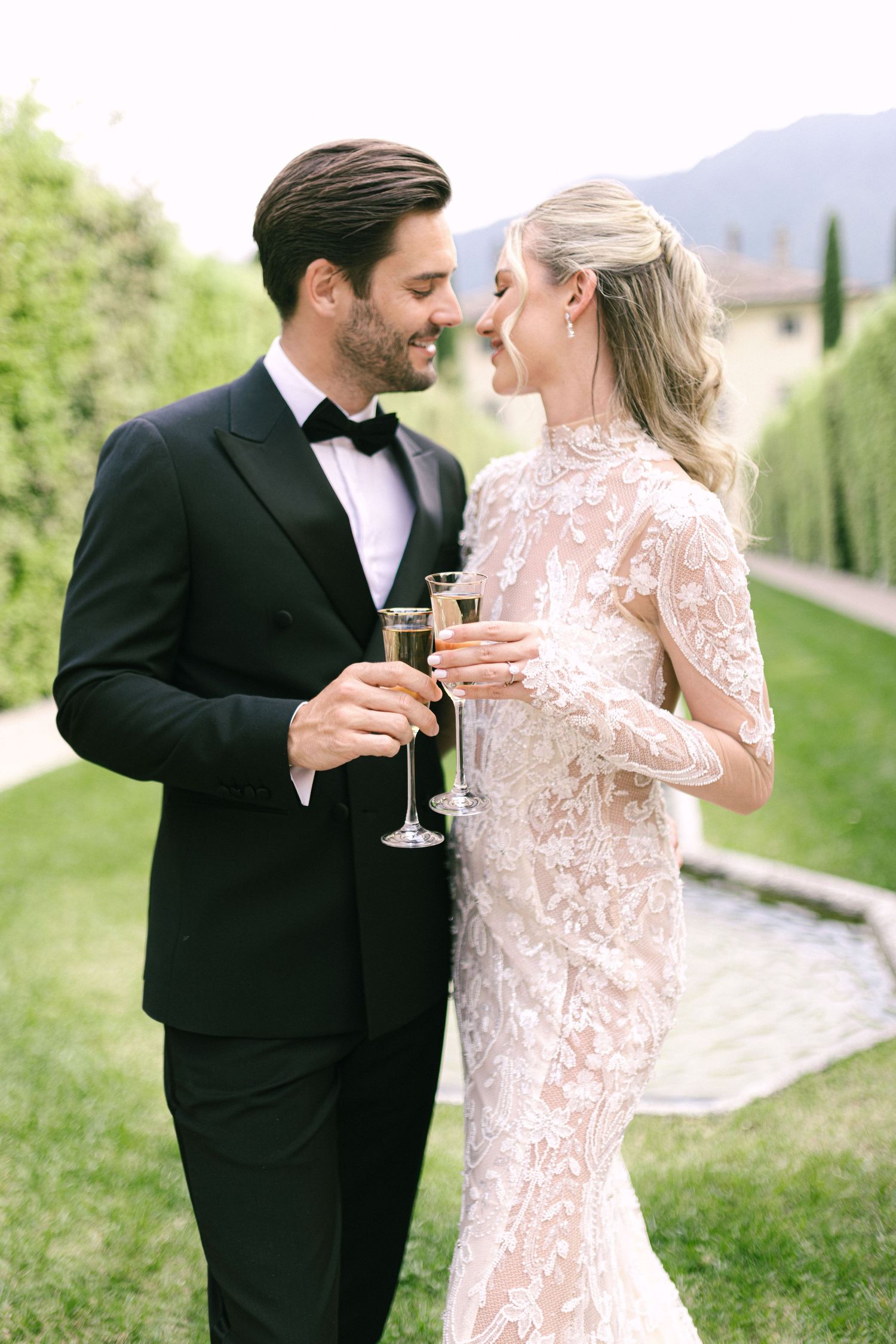 A couple in formal attire shares champagne together in an elegant outdoor garden setting.