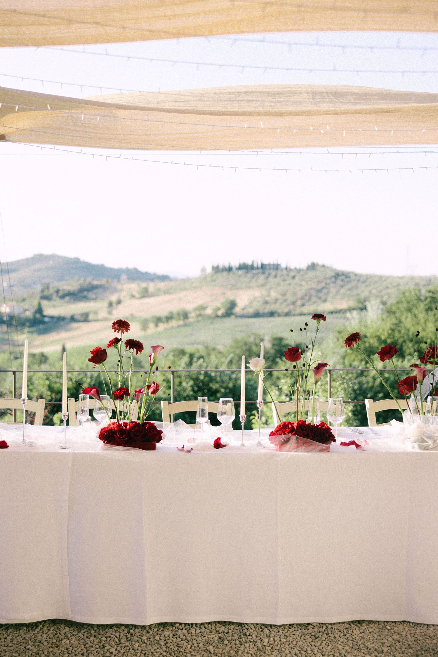 Elegant wedding reception table setup with red floral centerpieces against a scenic mountain backdrop.