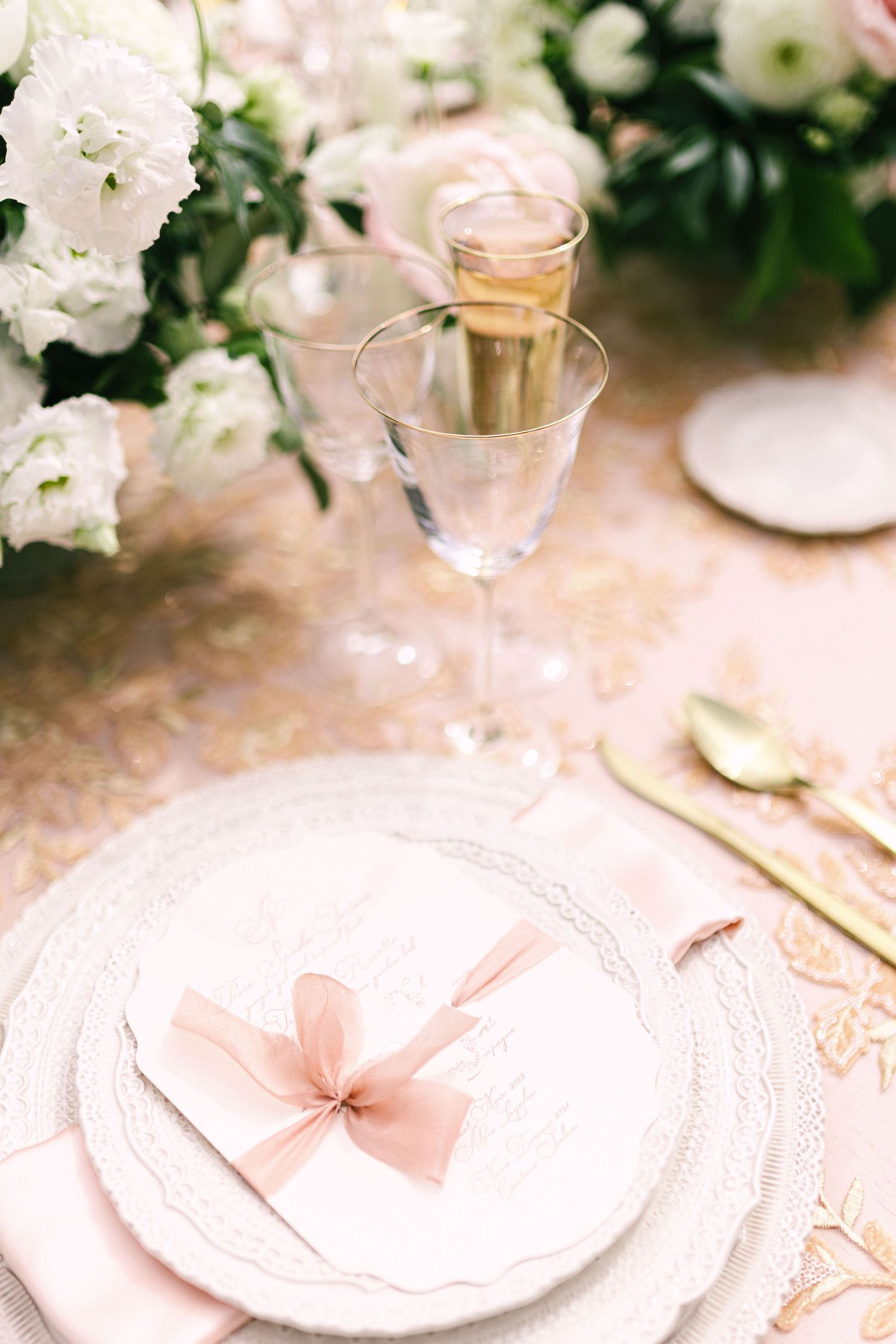 Elegant table setting with white plates, pink napkins, and delicate floral arrangements in soft pastel tones.