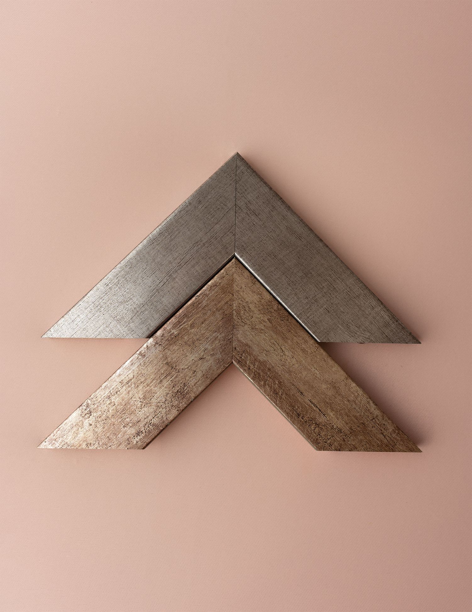 Two metallic silver and gold chevron-shaped frame pieces arranged in a V formation against a pale pink background.
