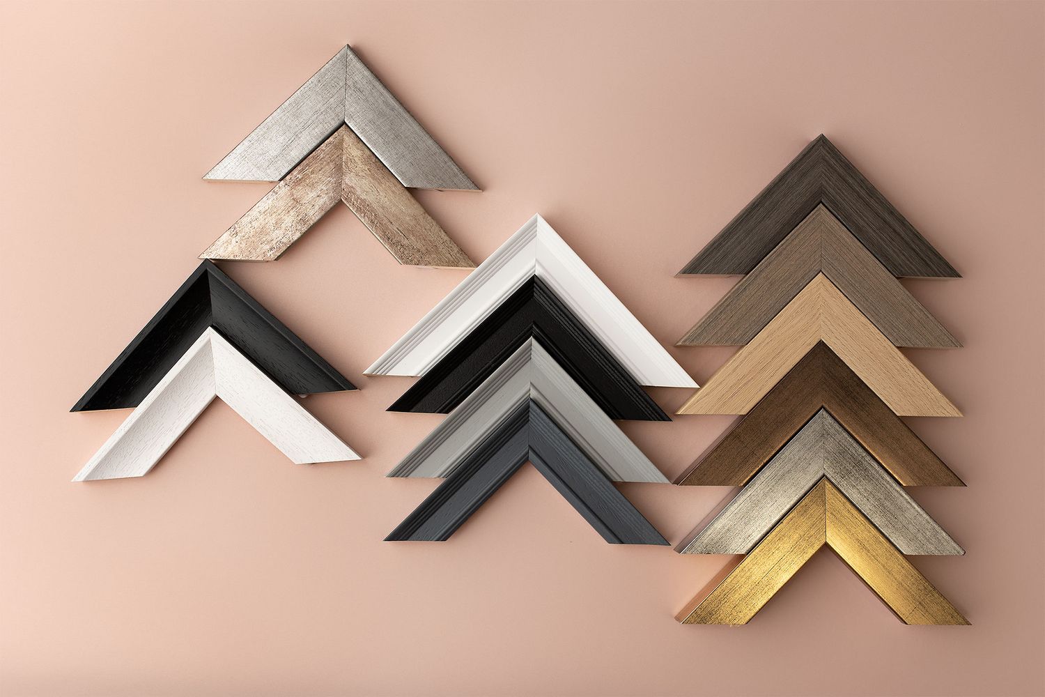 Modern picture frame corner samples in metallic finishes including gold, silver, black and white arranged on pink background.