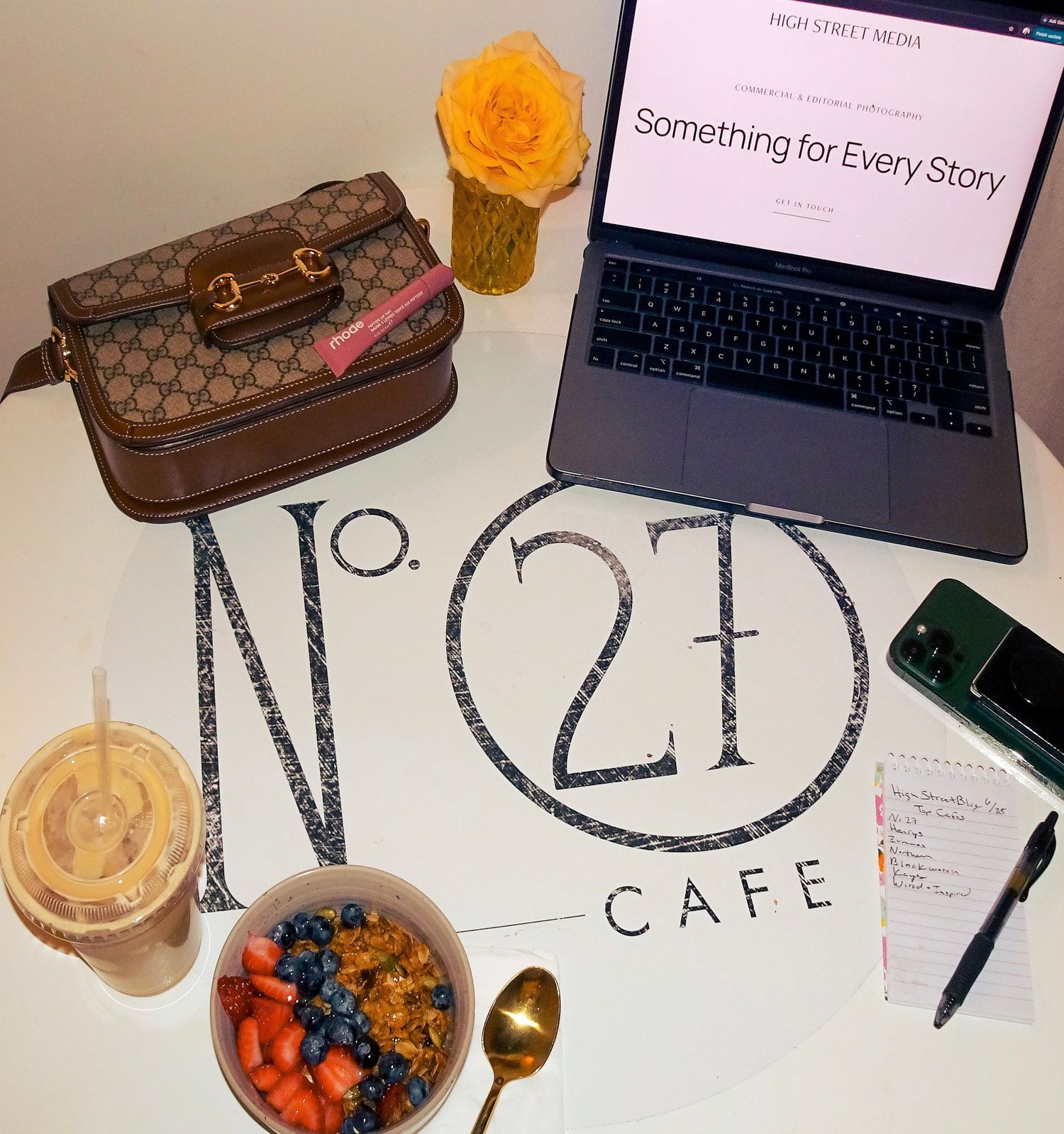 Overhead view of No. 27 Cafe table with Gucci bag, laptop, acai bowl, iced coffee, and notepad.