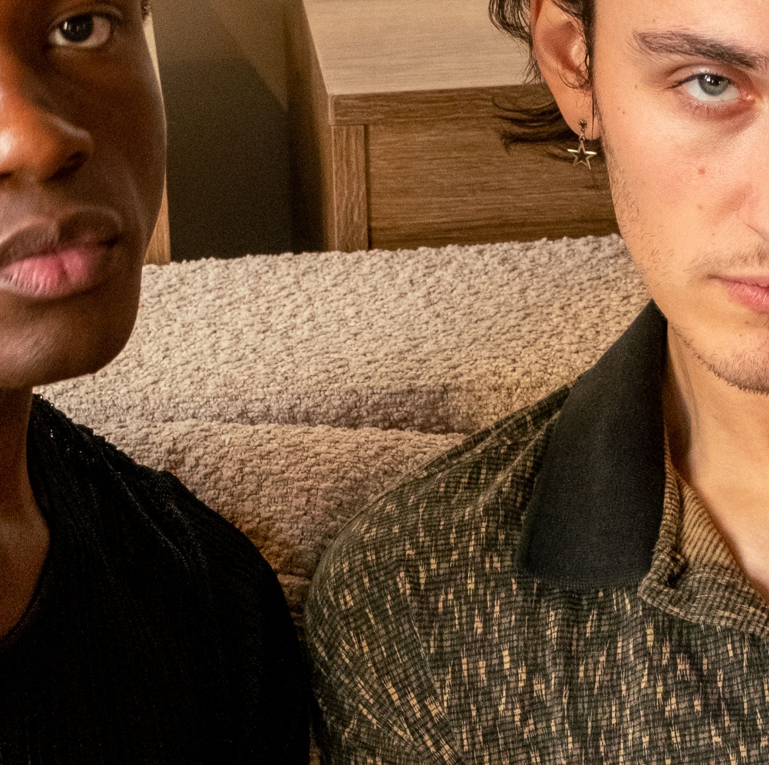 Two young men taking a close-up selfie indoors, one in black shirt and one in patterned shirt.