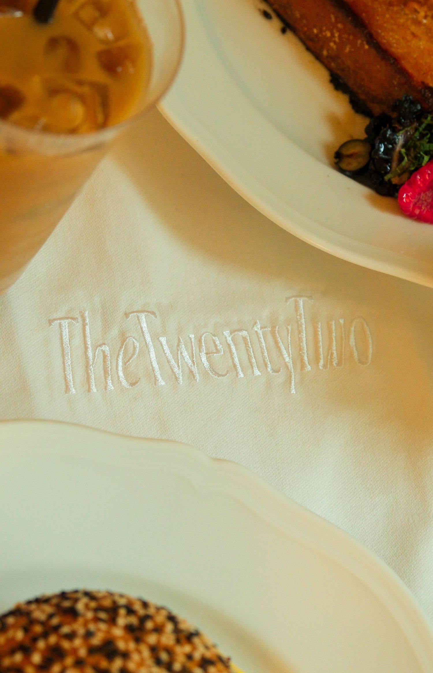 The Twenty Two New York embroidered white linen napkin with gourmet dishes on elegant dining table.