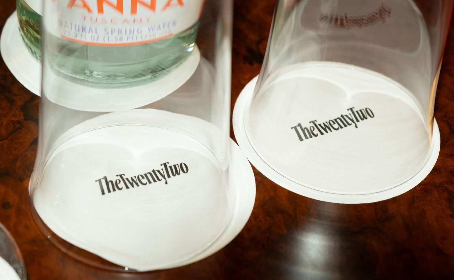 Two white coasters with The Twenty Two hotel logo on a wooden surface.