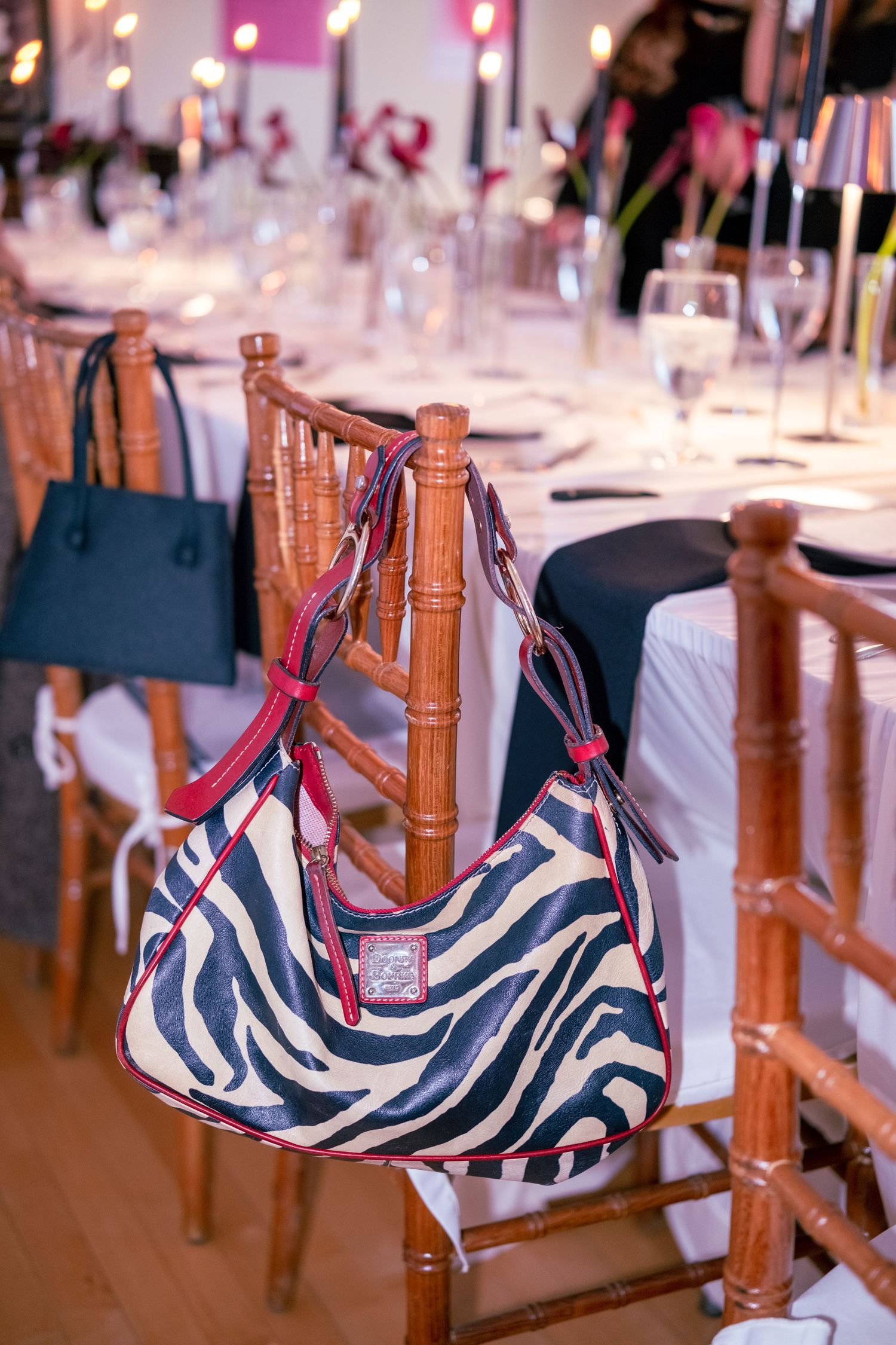 Zebra print handbag with red trim hanging on a bamboo chair at an elegant candlelit dinner event.